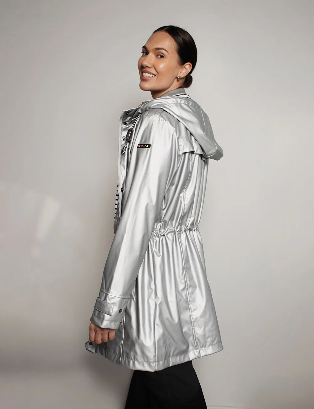 Woman wearing a silver raincoat against a plain background Shop Boetiek
