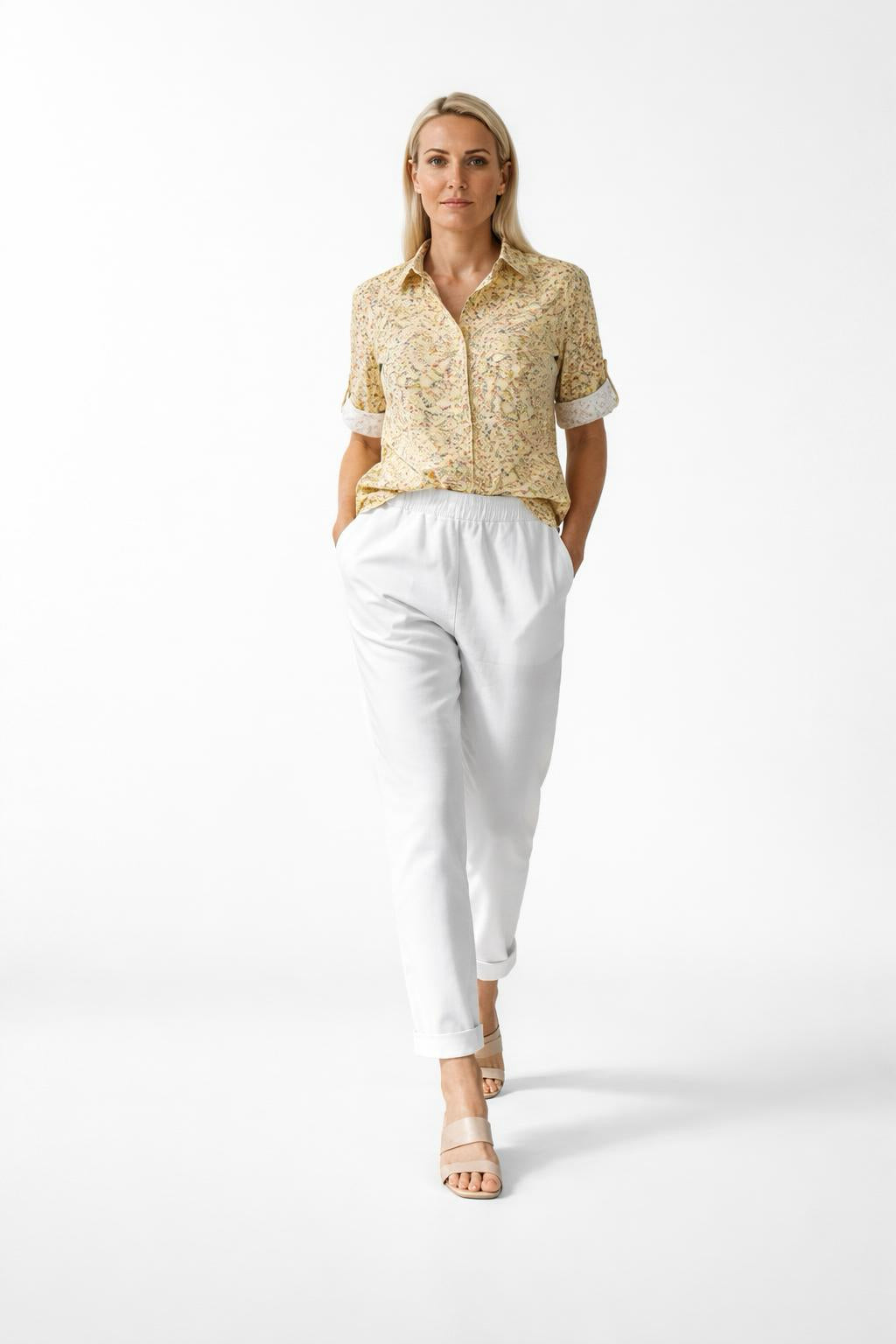 Woman wearing a yellow patterned blouse and white pants on a white background