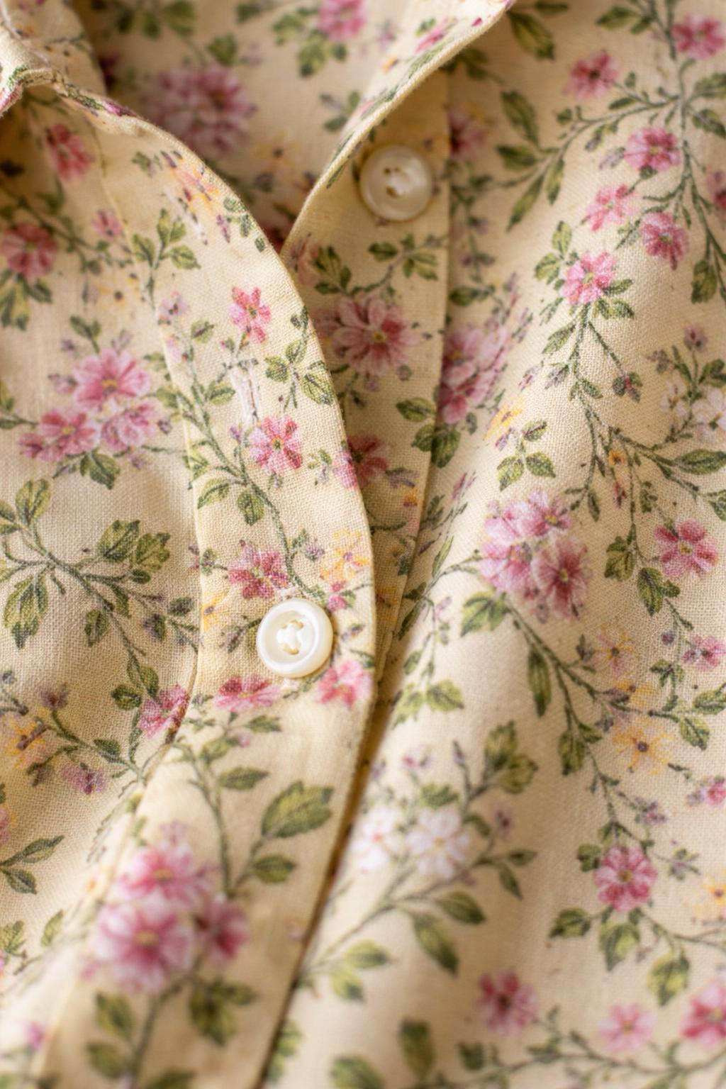 Close-up of a floral patterned fabric with pink and green flowers on a beige background.