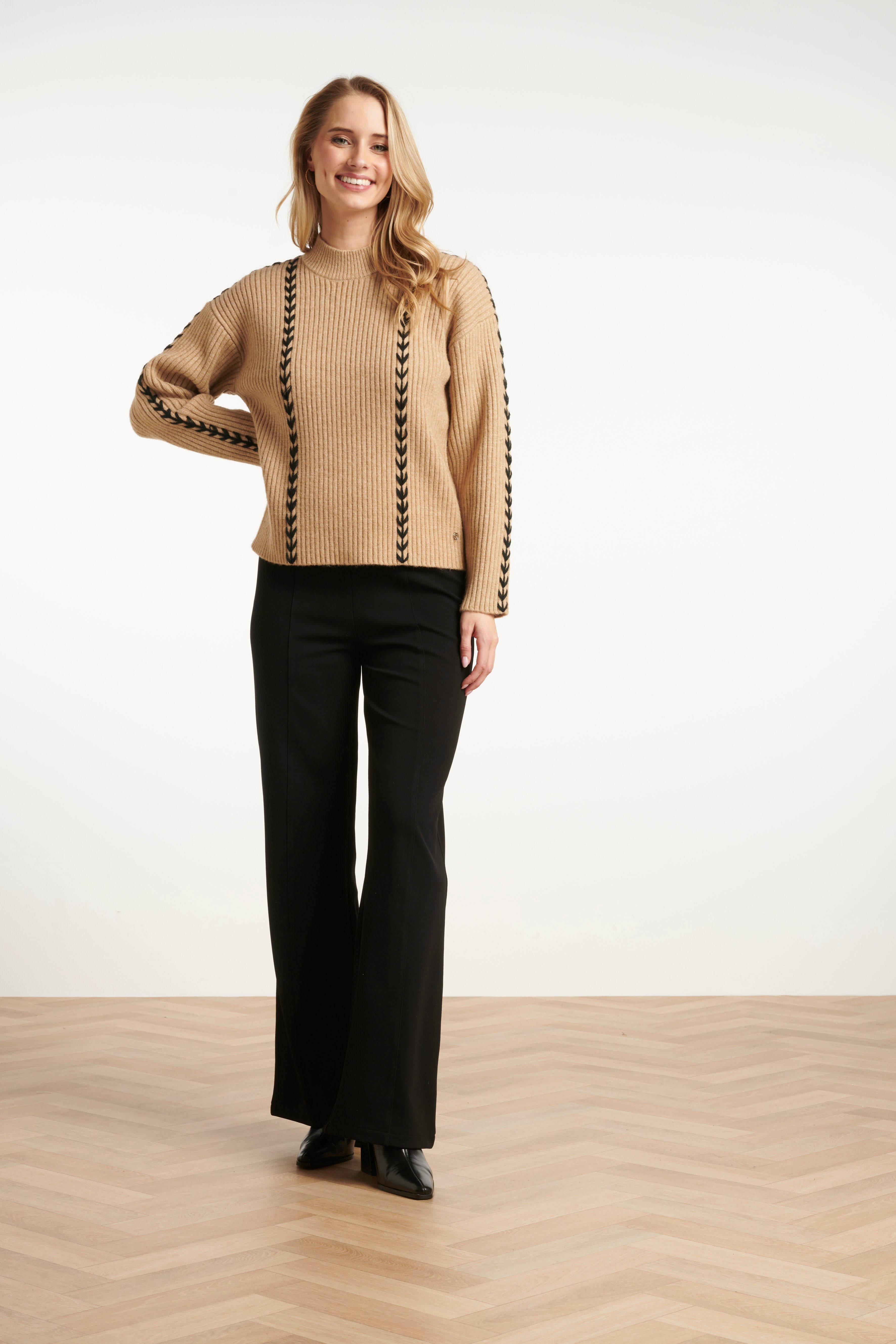 Smashed Lemon ribbed knit top in camel with black whipstitch contrast detailing, high neckline and long sleeves, front angled view with hand on shoulder