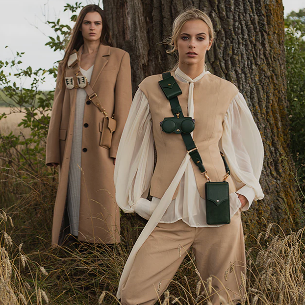 Two women in vintage-style clothing standing in a field with a large tree.