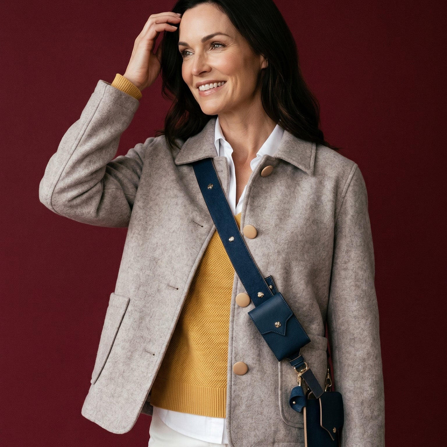 Woman wearing a beige jacket with a mustard shirt and white pants against a red background