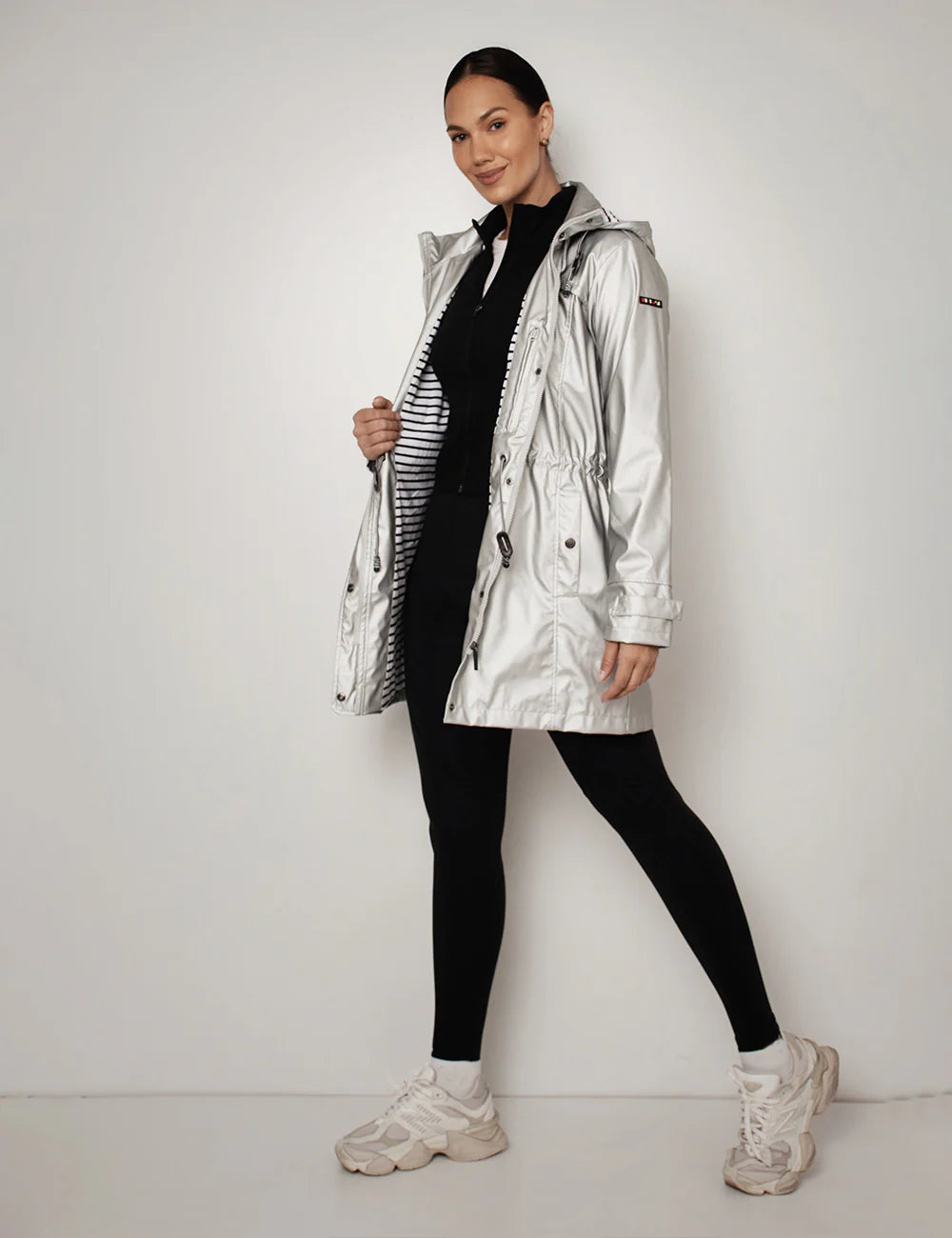 Person wearing a silver Batela jacket, black outfit, and white sneakers on a plain background Shop Boetiek