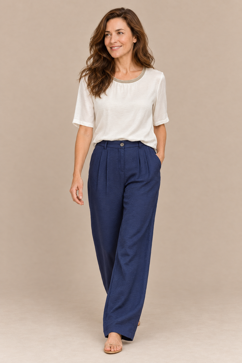 Model walking in the Andam navy pleated wide leg satin pants worn with the Crudo satin blouse