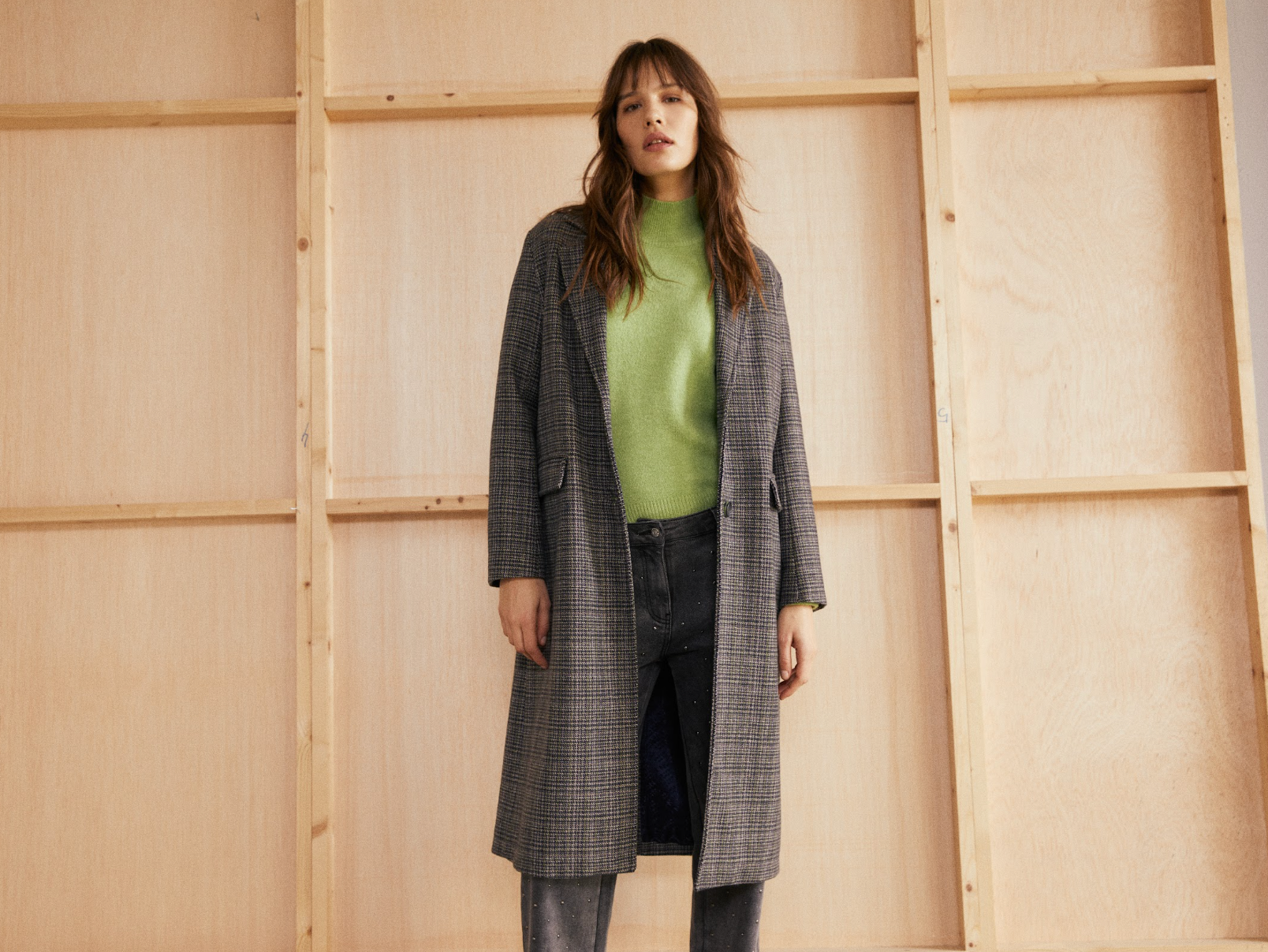 Model wearing the Andam knit jumper in green styled with a checked coat and embellished charcoal jeans.