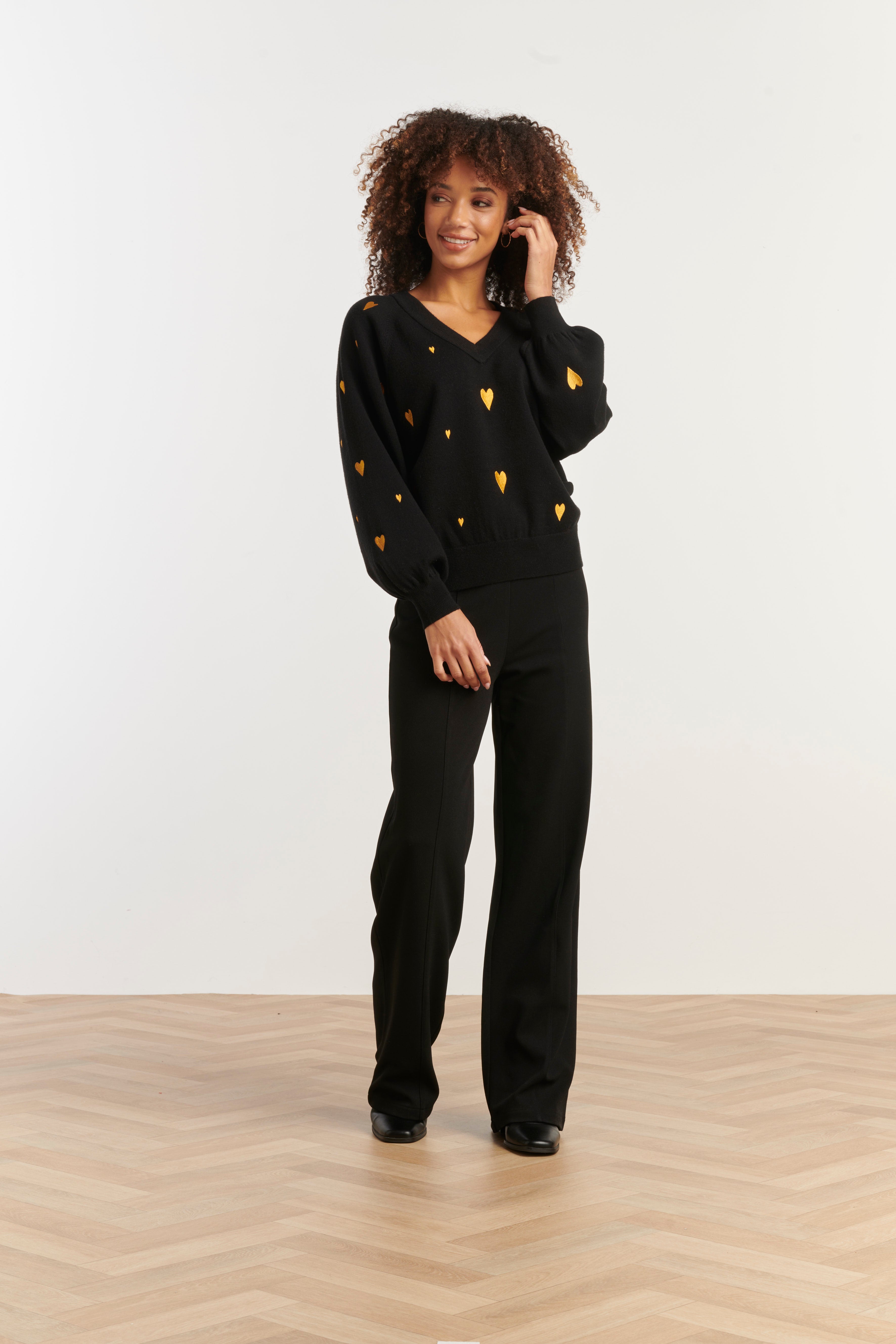 Smashed Lemon V-neck knit top in black with scattered gold heart print, long sleeves, front view with hand at face