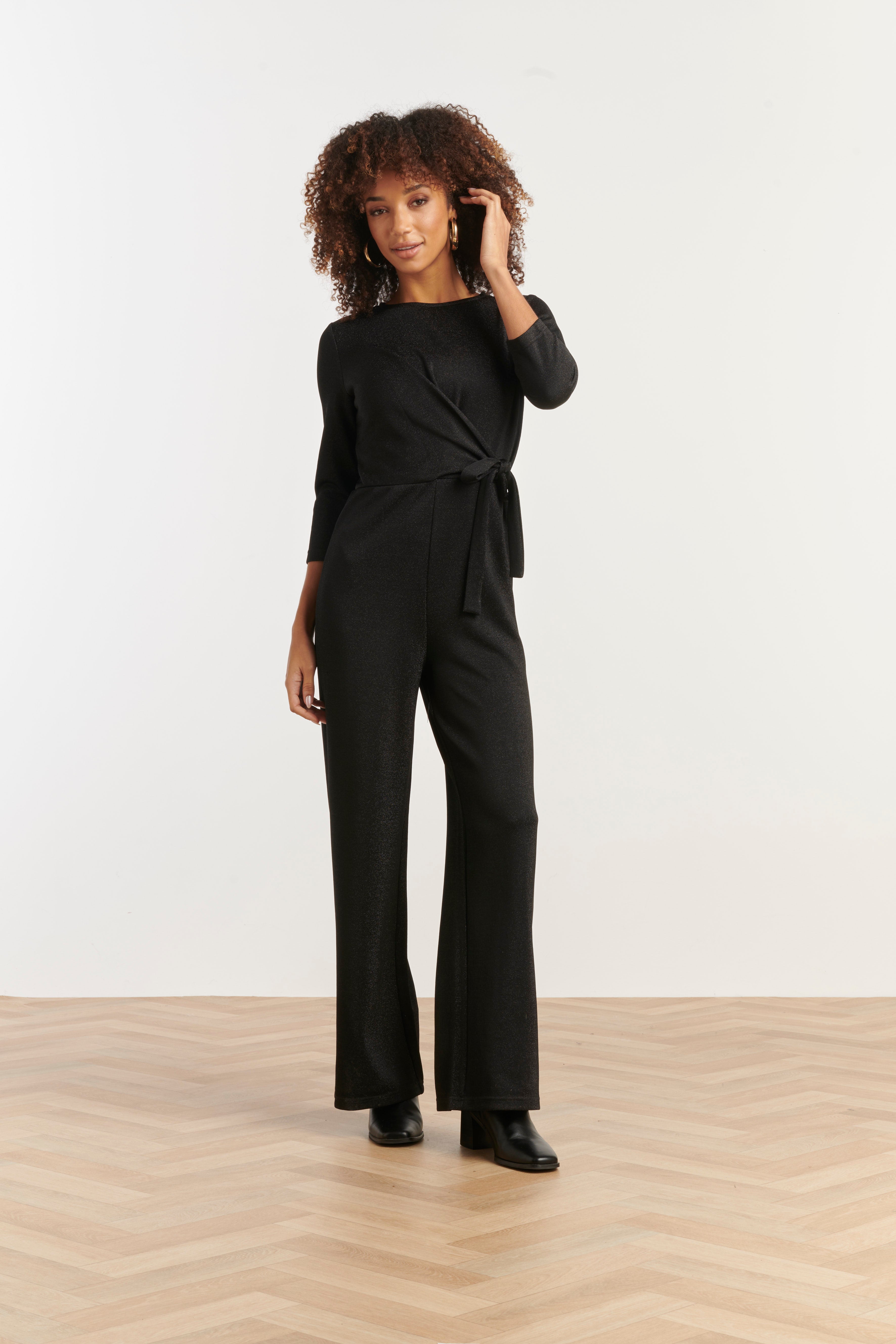 Smashed Lemon wrap jumpsuit in black with three-quarter sleeves and wide leg, front view with hand at face