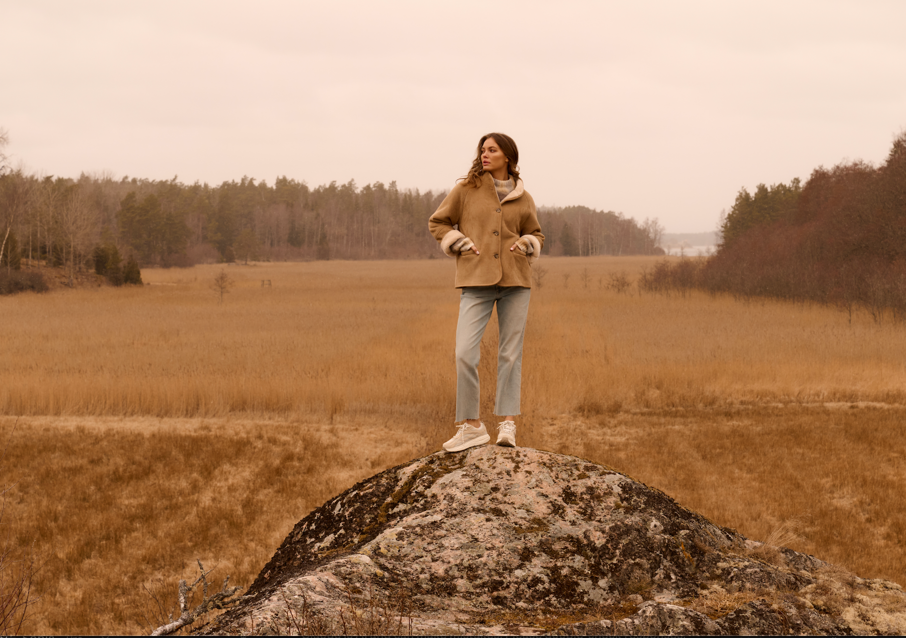 Model wearing the YAYA Faux Lammy Coat with Raglan Sleeves in sand styled with light-wash denim in an outdoor countryside setting.