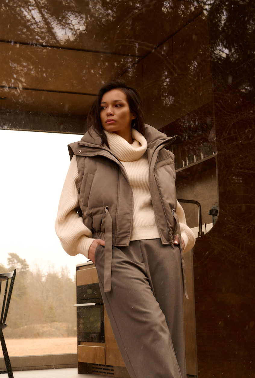 Model wearing the YAYA Oversized Cropped Jacket with Detachable Sleeves in grey, layered over a cream knit with tailored trousers in a modern architectural setting.